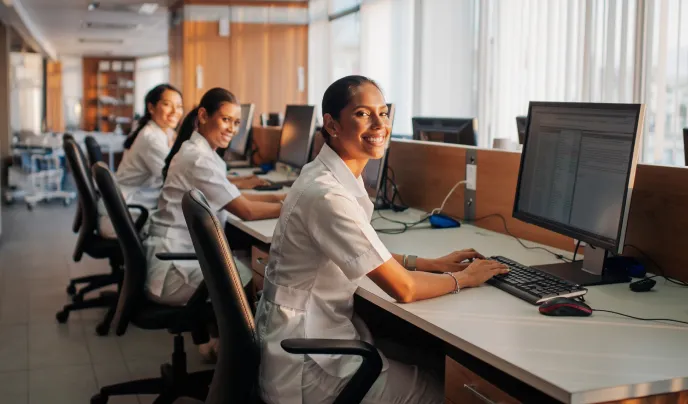 Three women in white scrubs sitting at computers