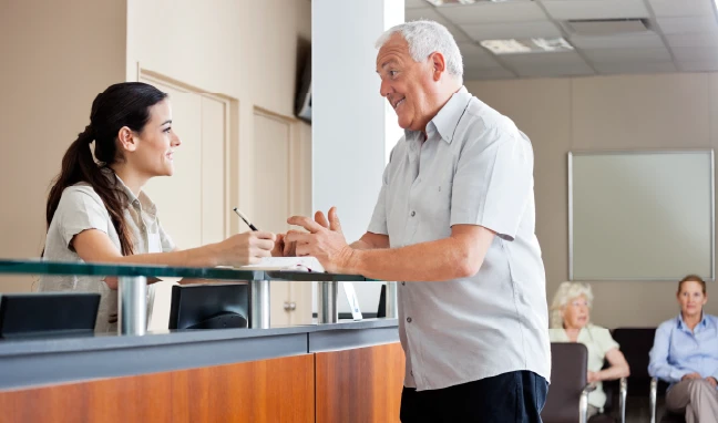 man speaking to receptionist at hospital front desk